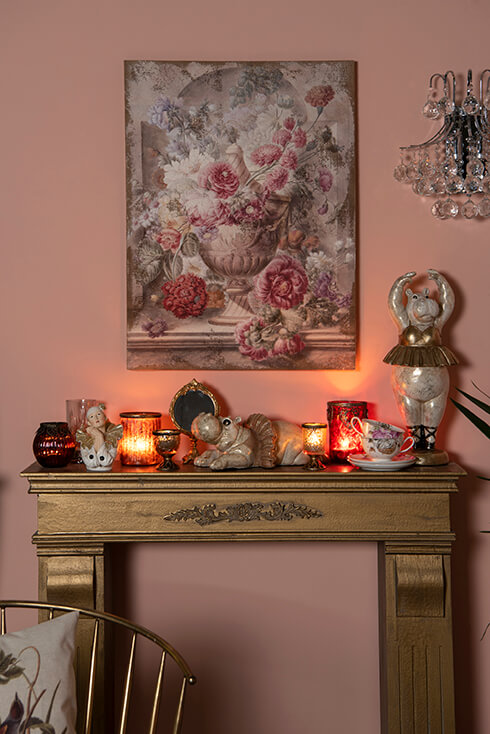 A mantelpiece with sculptures and burning candles, with a painting of flowers in the background