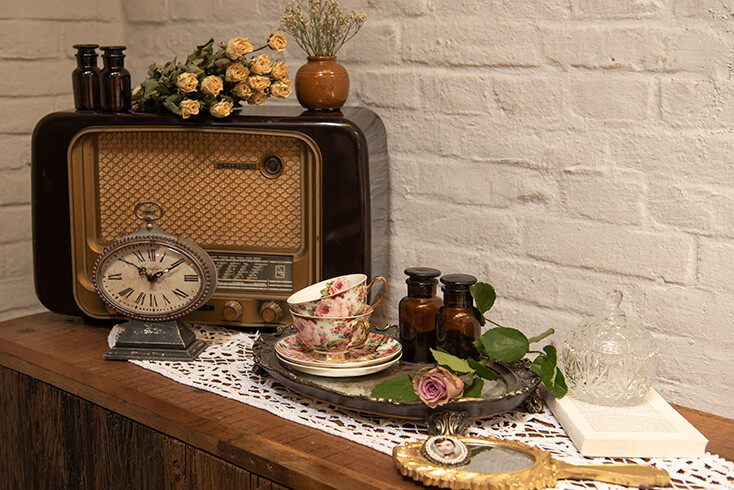 Uno specchio da mano, un vassoio con tazze e piattini e accanto un piccolo orologio da tavolo per una vecchia radio