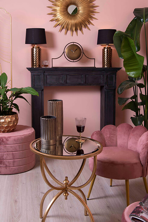 Un tavolino moderno con pouf rosa intorno e sullo sfondo un orologio da tavolo su un caminetto