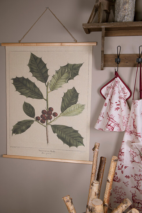 A wall tapestry of a branch with an apron, a pot holder, and a napkin alongside