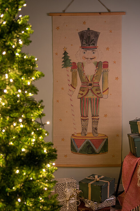 In the foreground, a Christmas tree and presents, and in the background a wall tapestry of a nutcracker