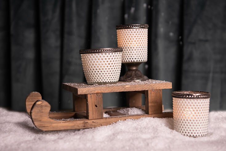Ein Holzmini-Schlitten, auf dem weiße Teelichthalter in einer Schicht Kunstschnee stehen