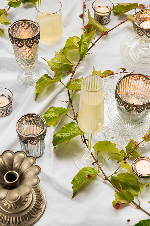 Ein gedeckter Tisch mit Glas- und romantischen Teelichthaltern sowie einem Champagnerglas