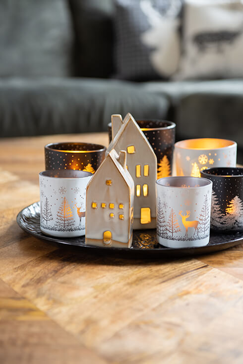 Ein schwarzes Metalltablett mit weihnachtlichen Teelichthaltern und zwei Keramikhäusern mit Kerzen