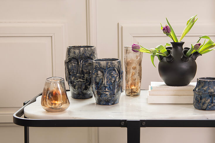 Ein Marmortisch mit zwei blauen Blumentöpfen, zwei braunen Vasen und einer schwarzen Tulpenvase mit violetten Tulpen
